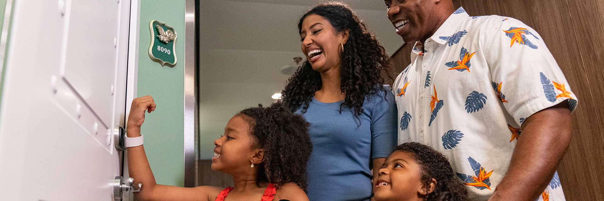 Two adults and two children standing at a stateroom door, with one child scanning her magic band while holding plush toys.