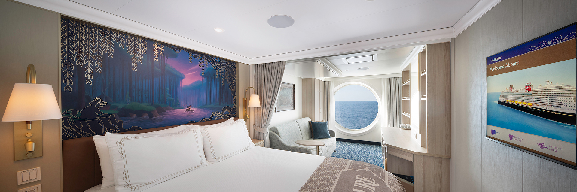 Cruise ship stateroom with a queen bed, themed wall art, seating area, and a round porthole window overlooking the ocean.